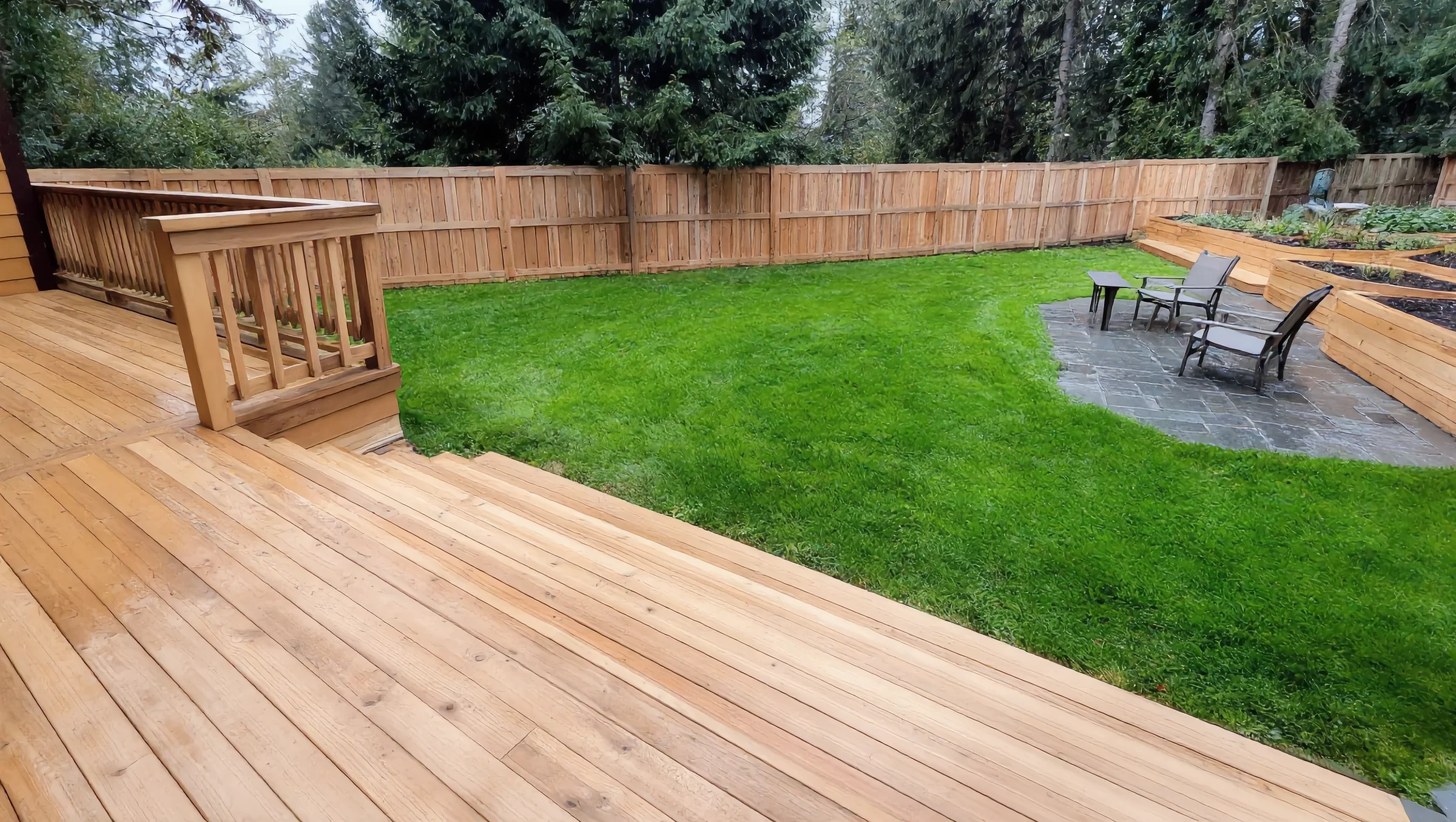 New wood deck overlooking a lawn, stone patio, fence and raised garden beds